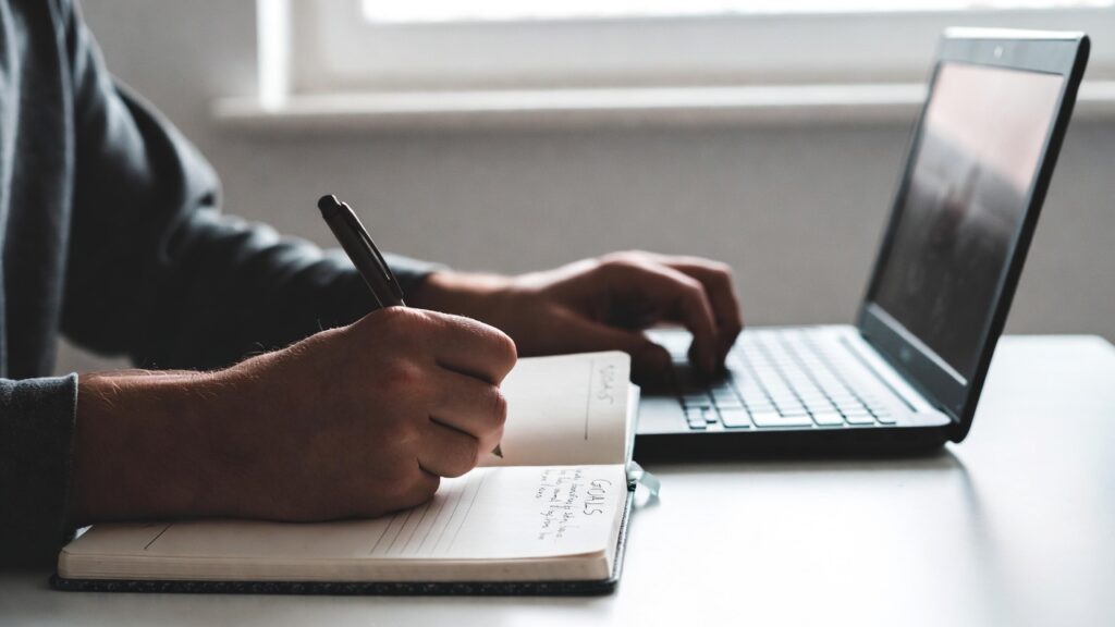 Escolhas que Transformam Seu Futuro: 7 Decisões que Podem Mudar Sua Vida Para Sempre 15 Pessoa escrevendo metas em um caderno organizado sobre mesa minimalista